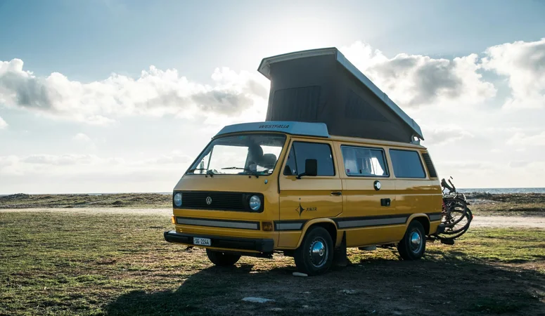 Yellow VW bus camper van with high roof and two e-bikes mounted on the tailgate.