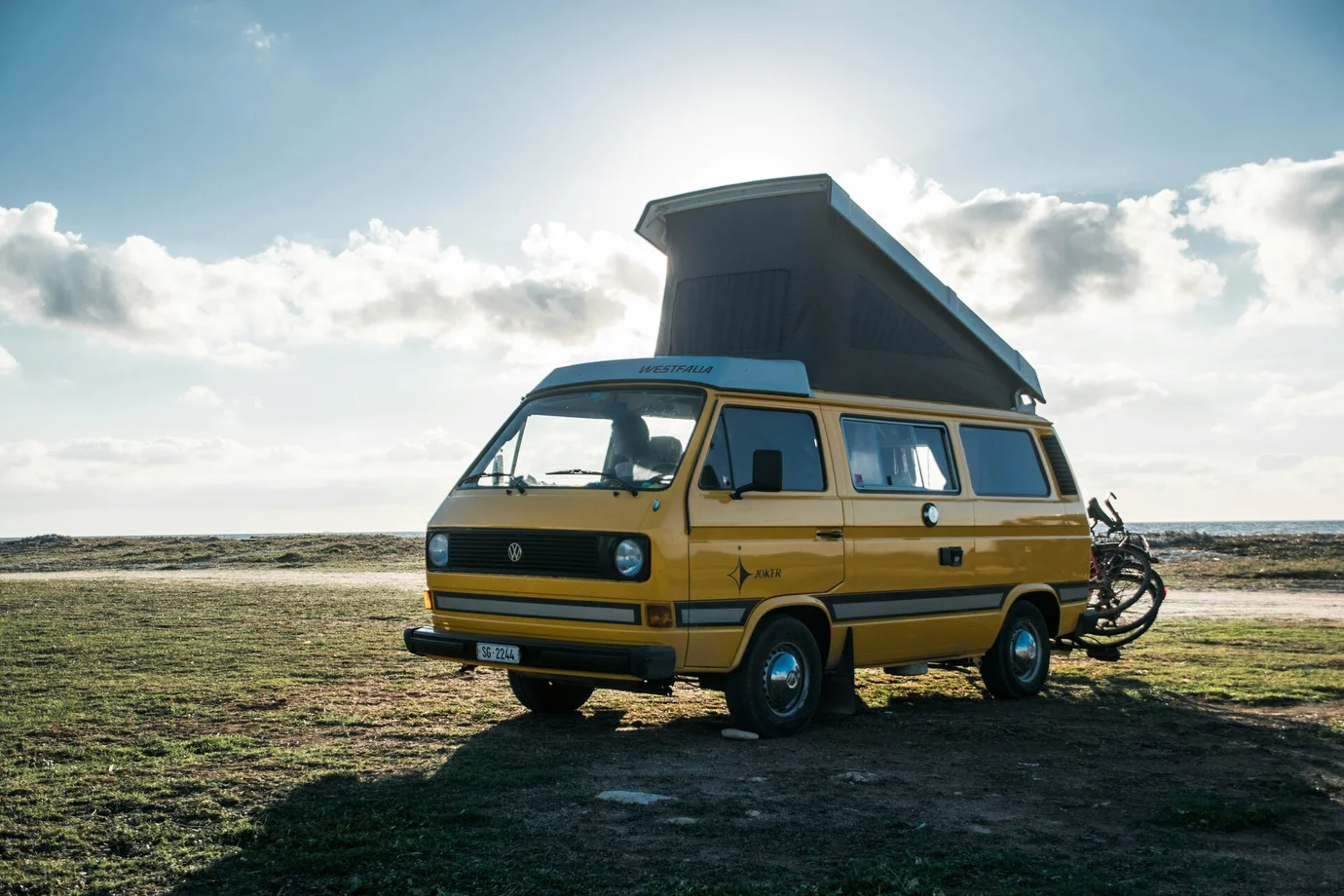 Yellow VW bus camper van with high roof and two e-bikes mounted on the tailgate.