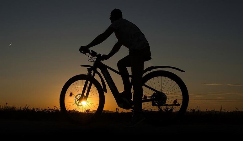 Elektrofahrrad vor Sonnenuntergang. Der Fahrer fragt sich vielleicht gerade, wie er seinen E-Bike Akku richtig laden kann.