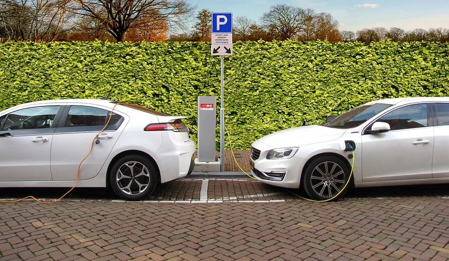 Two white electric cars being charged. Once they have done their duty, they and the lithium-ion batteries have to be disposed of.